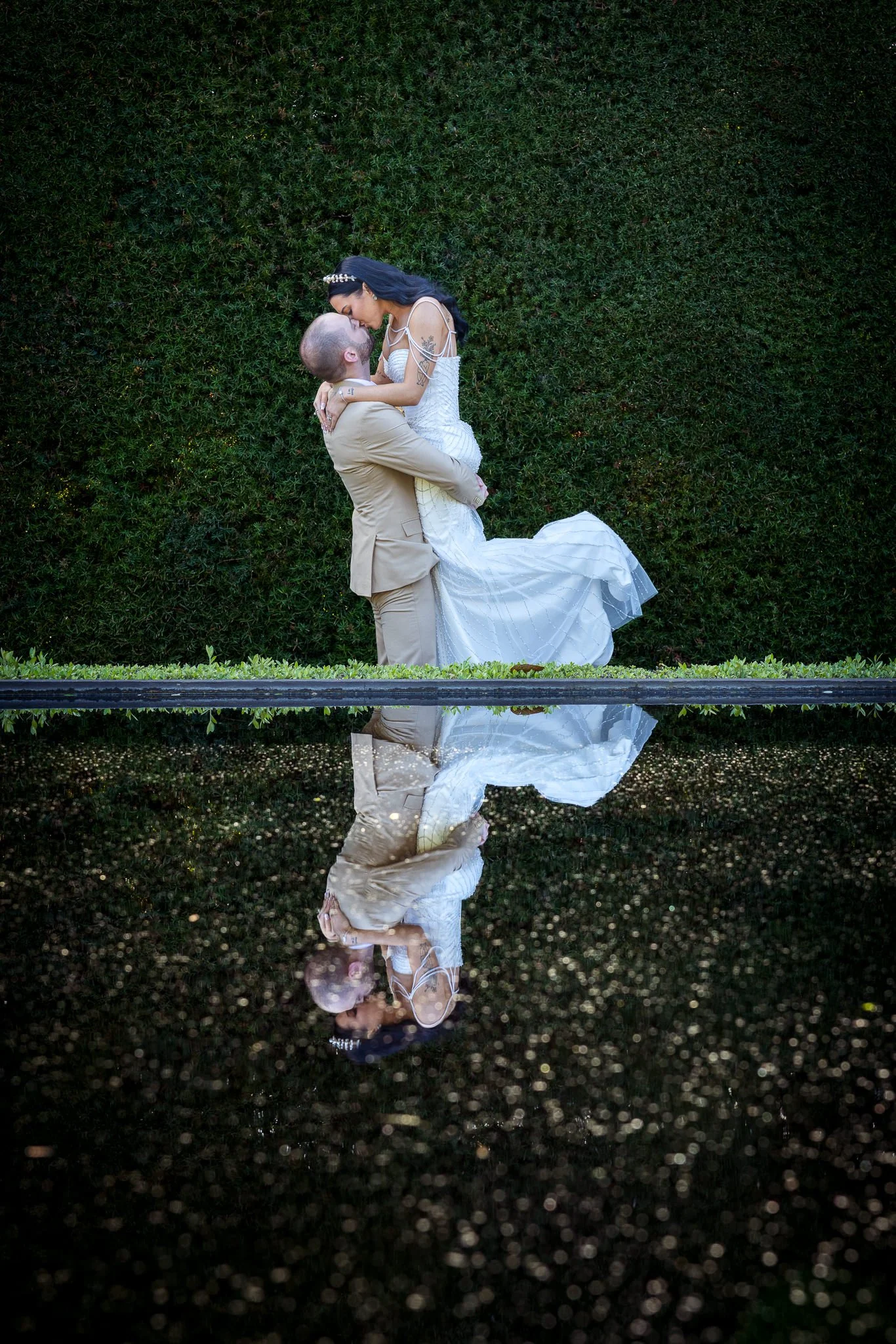 A groom lifts his bride, reflected in a pool at night