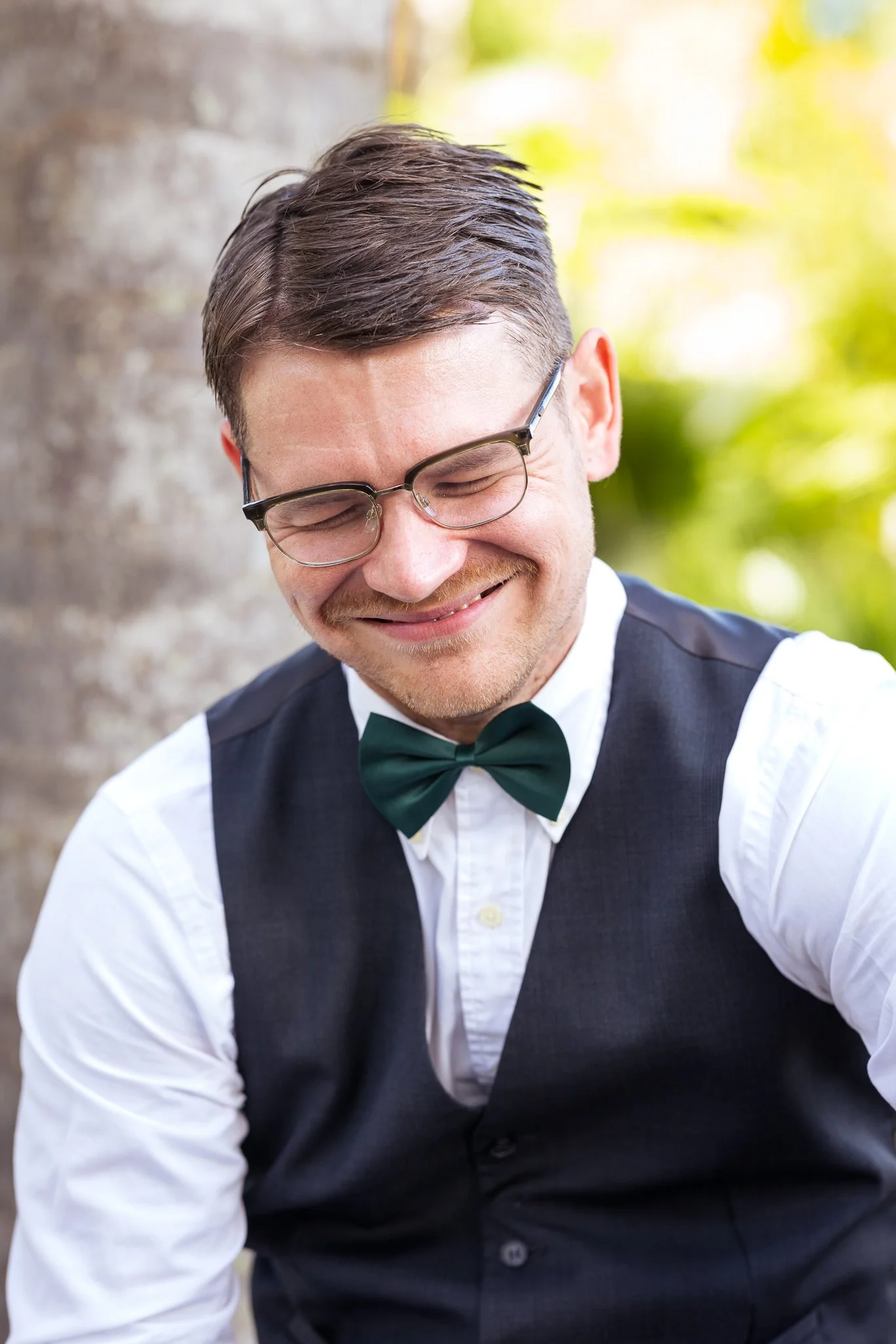 A groomsman in a bow tie laughs and looks down