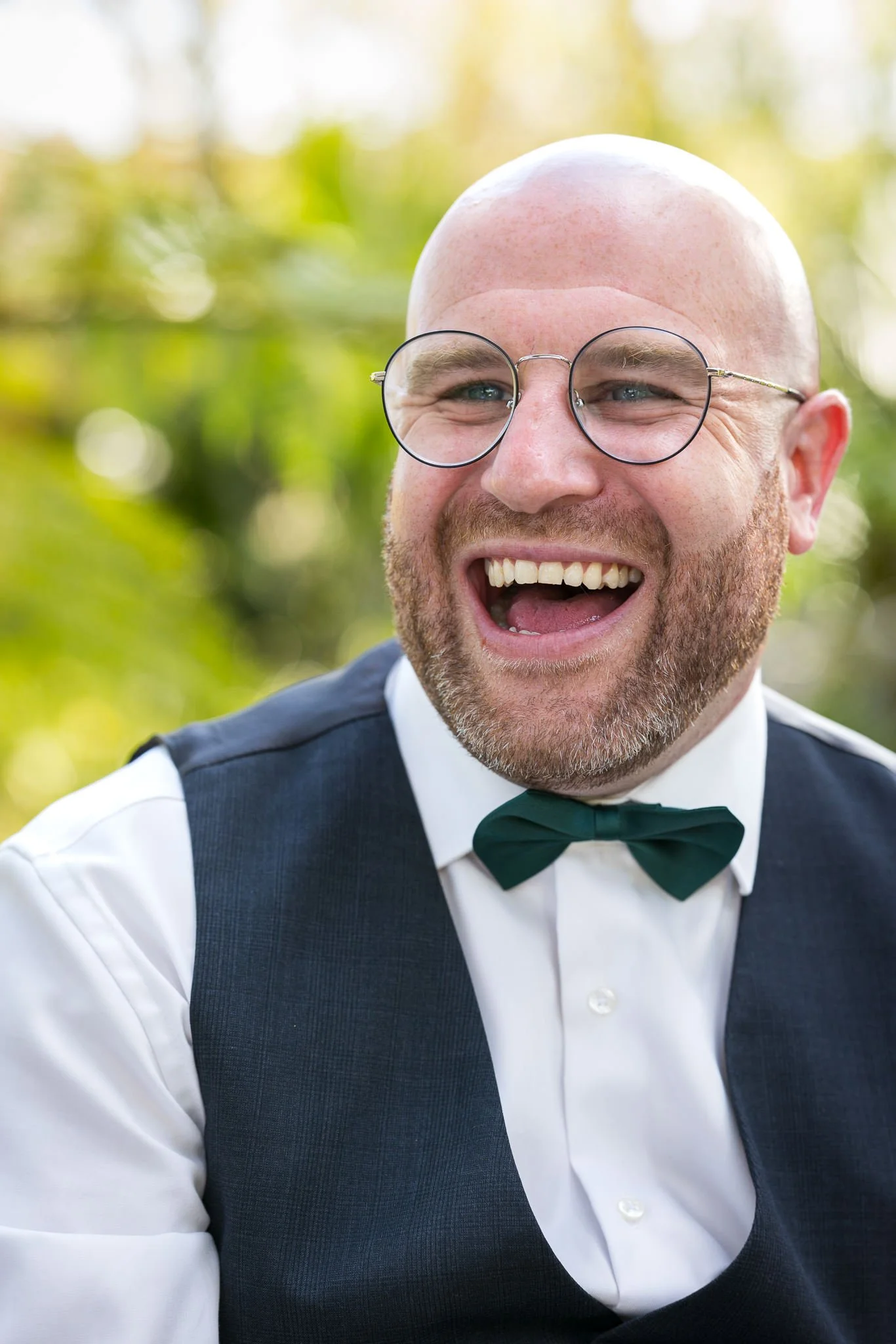 A groomsman in round glasses laughs heartily
