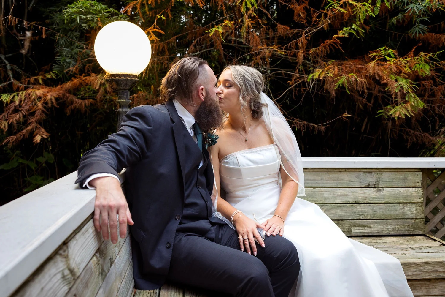 Felicity and Ronan kiss on a garden bench beside a lamp