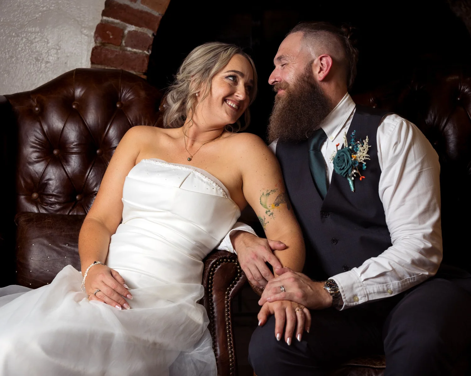 Felicity and Ronan smile at each other on a leather chesterfield