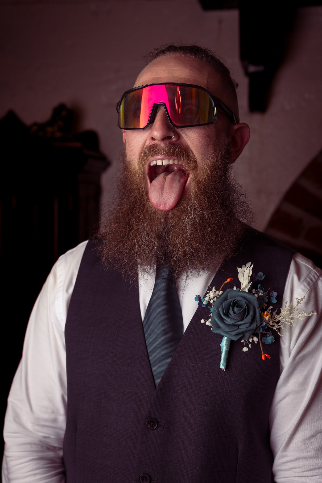 A groomsman in sunglasses sticks his tongue out for the camera