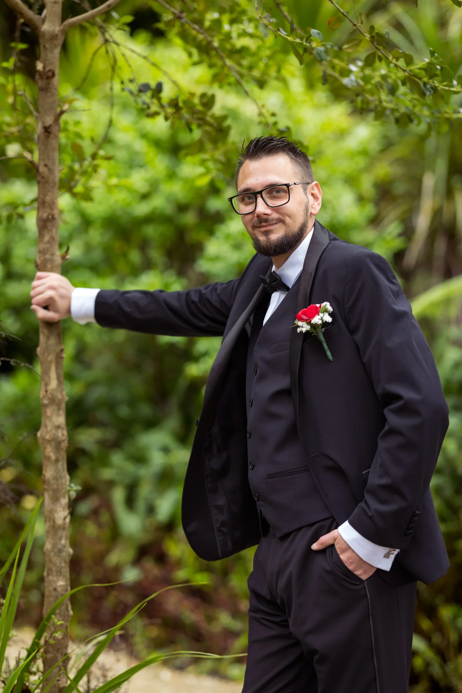Nick leans against a tree in his tuxedo