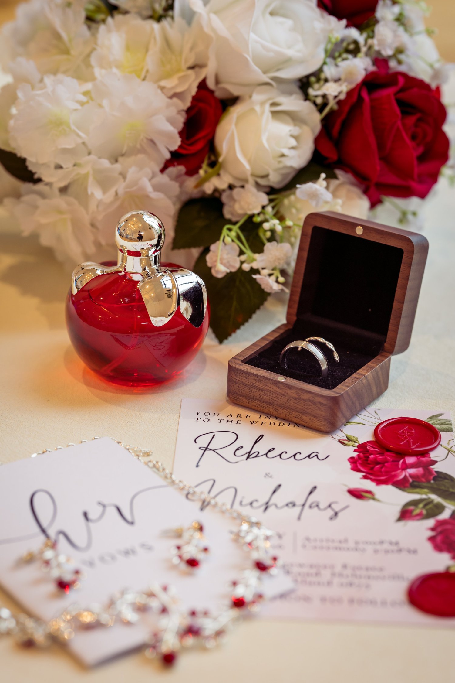 Rebecca's perfume, ring box and invitation among red and white roses