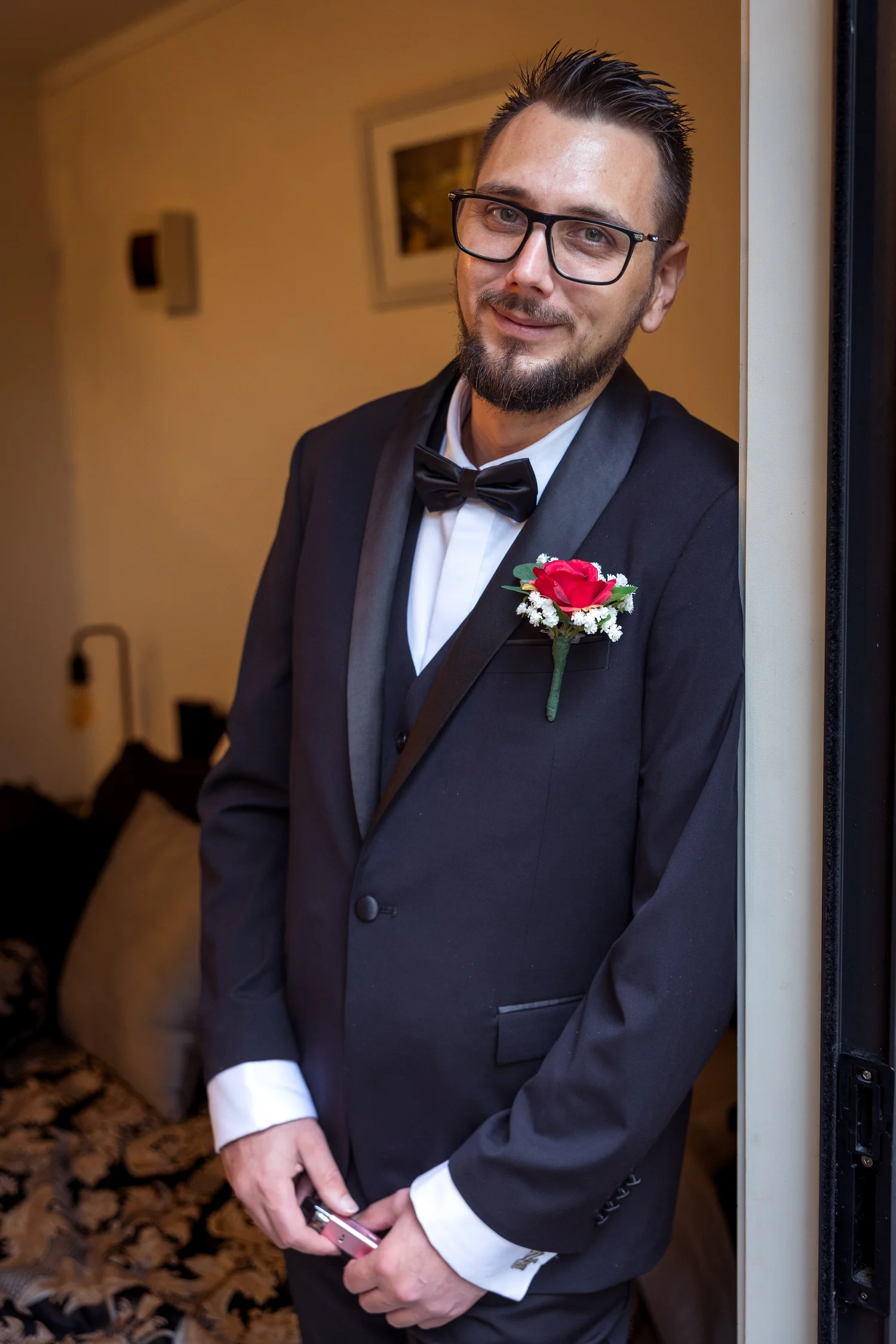 Nick smiles in his tuxedo by a doorway