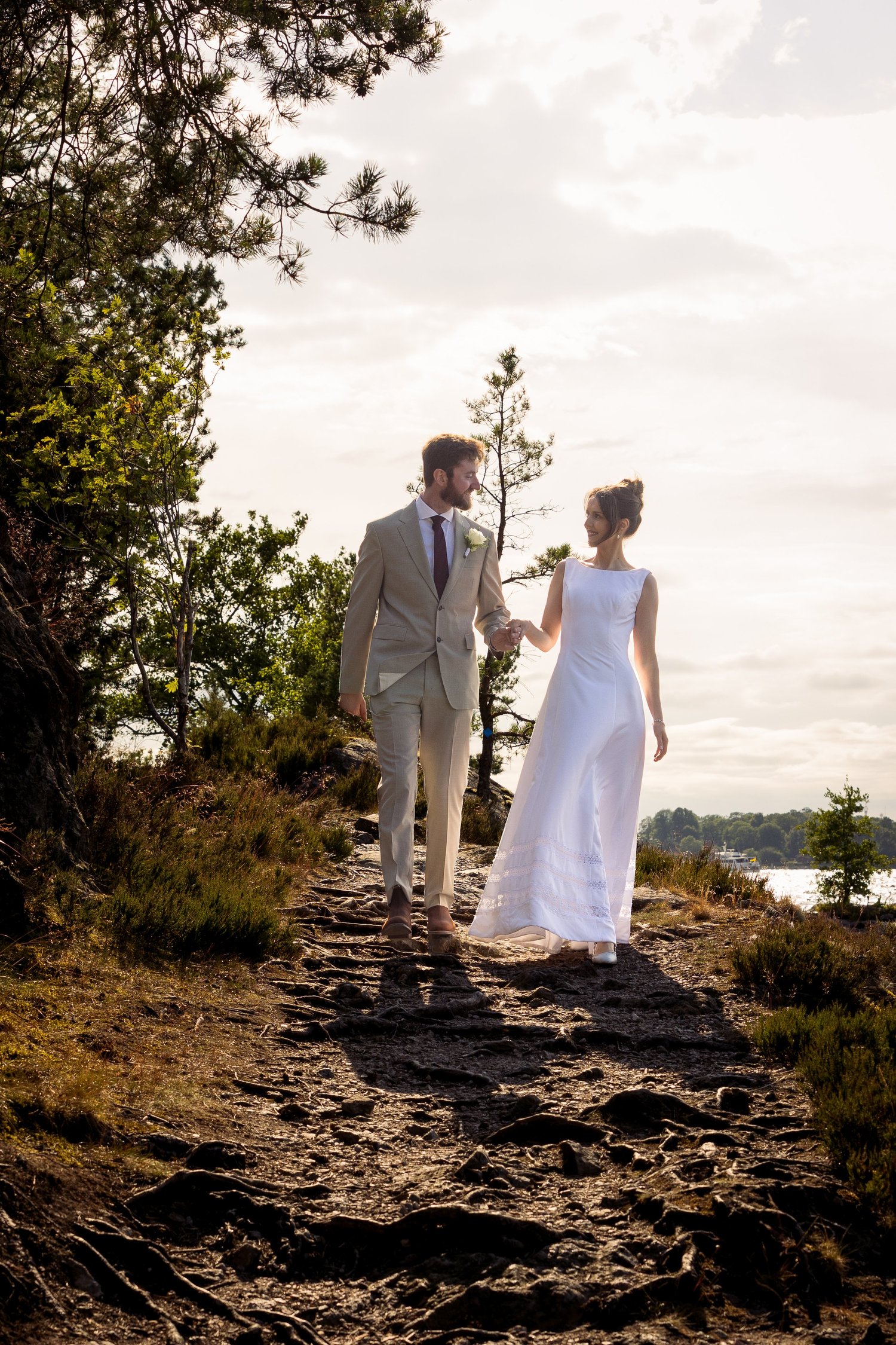 Sofia and John walk along a rocky path towards the water at sunset