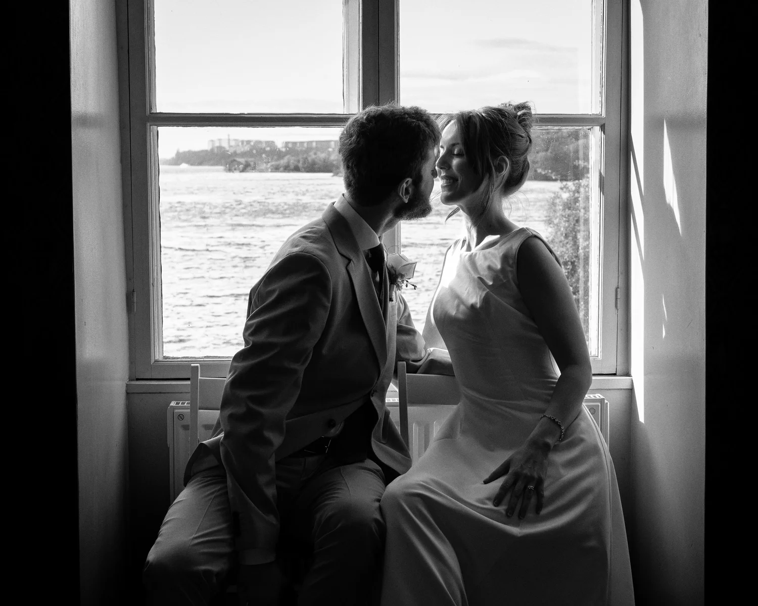 Black and white photo of Sofia and John kissing by a window