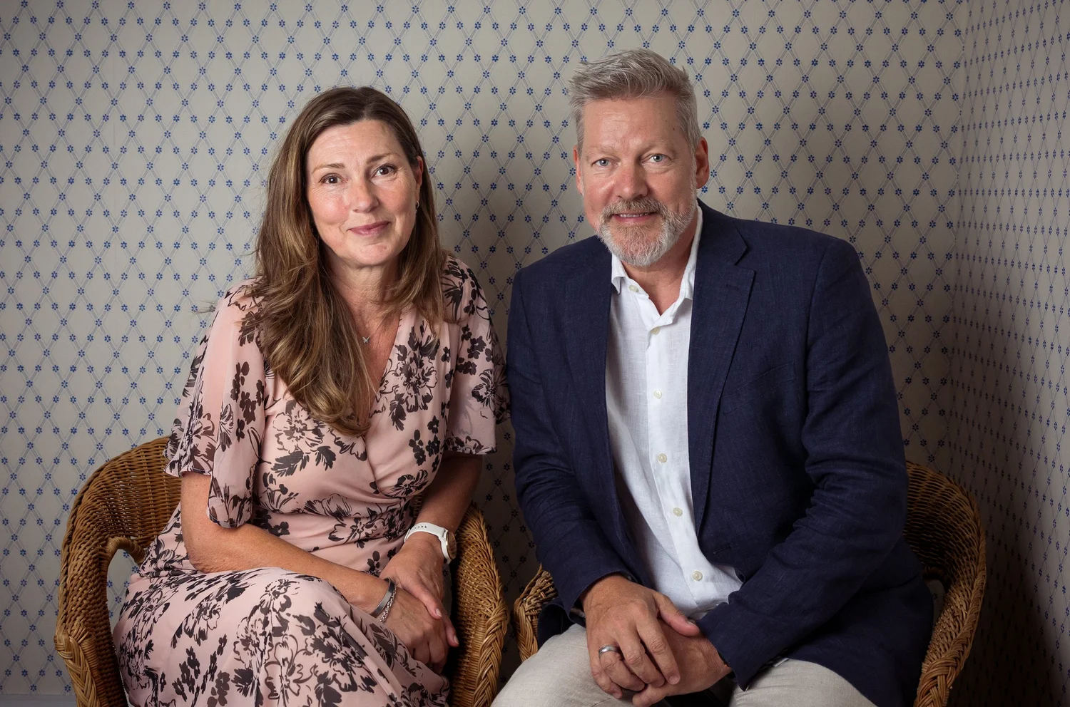 Two guests seated for a portrait against patterned wallpaper