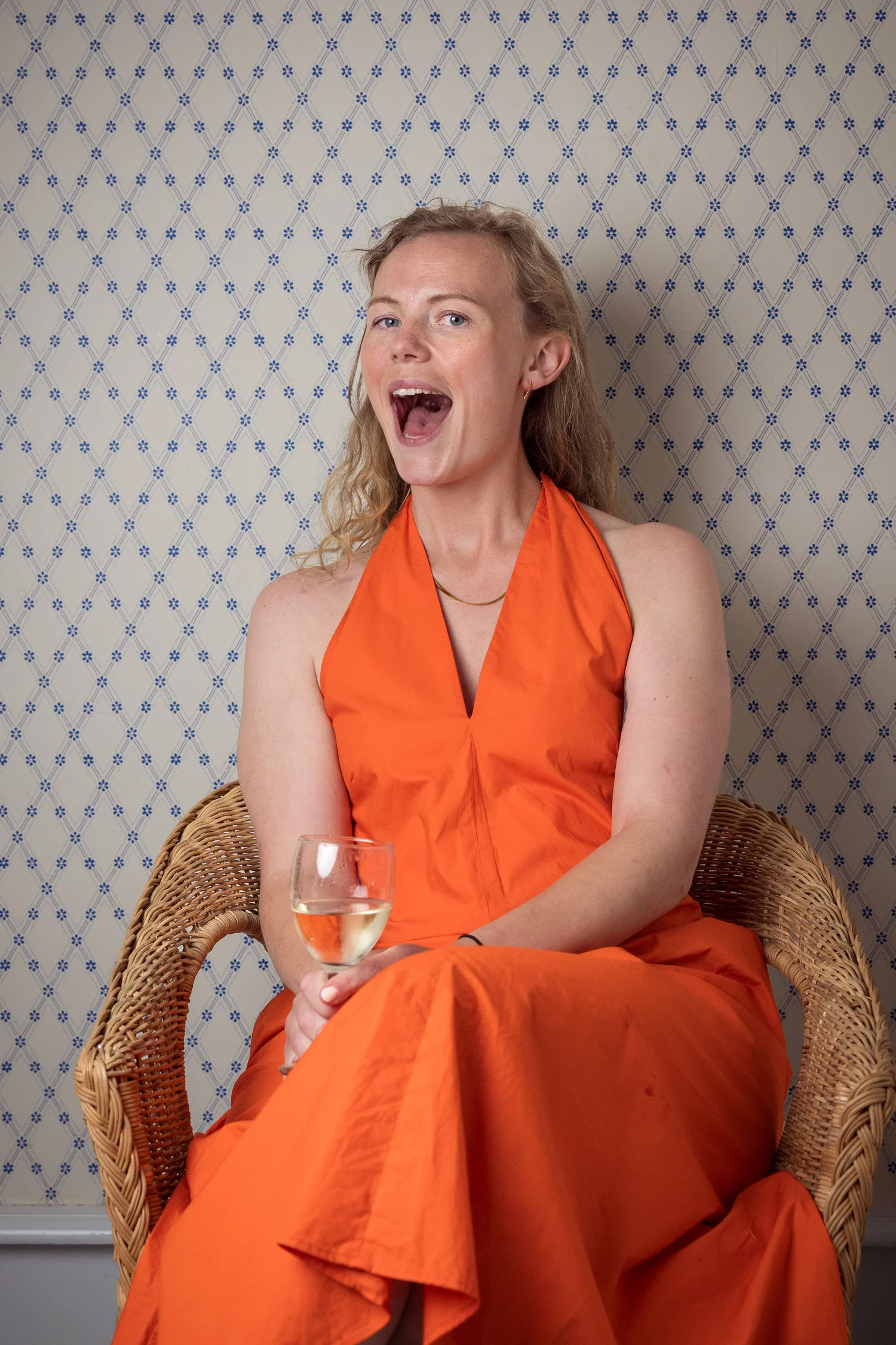 A guest in an orange dress laughs in a wicker chair