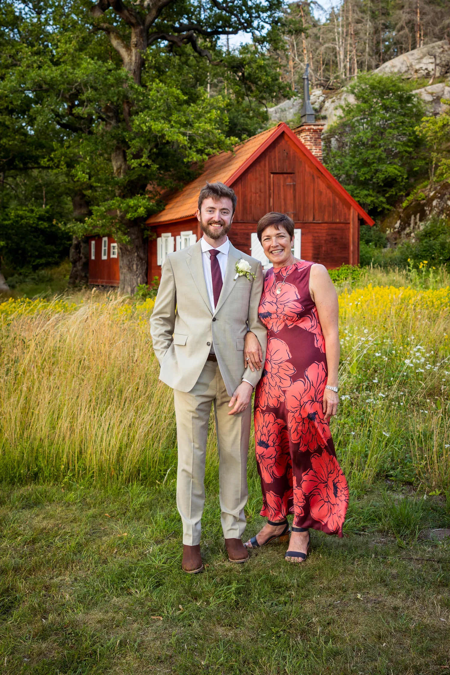 John stands with a guest in the meadow in front of a red cottage
