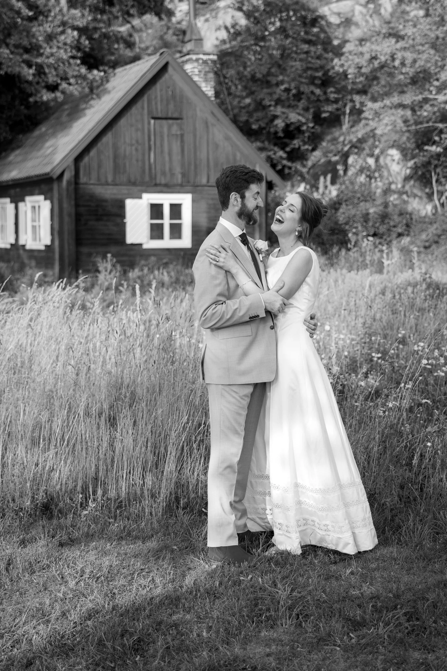 Black and white photo of Sofia and John in long grass by a cottage