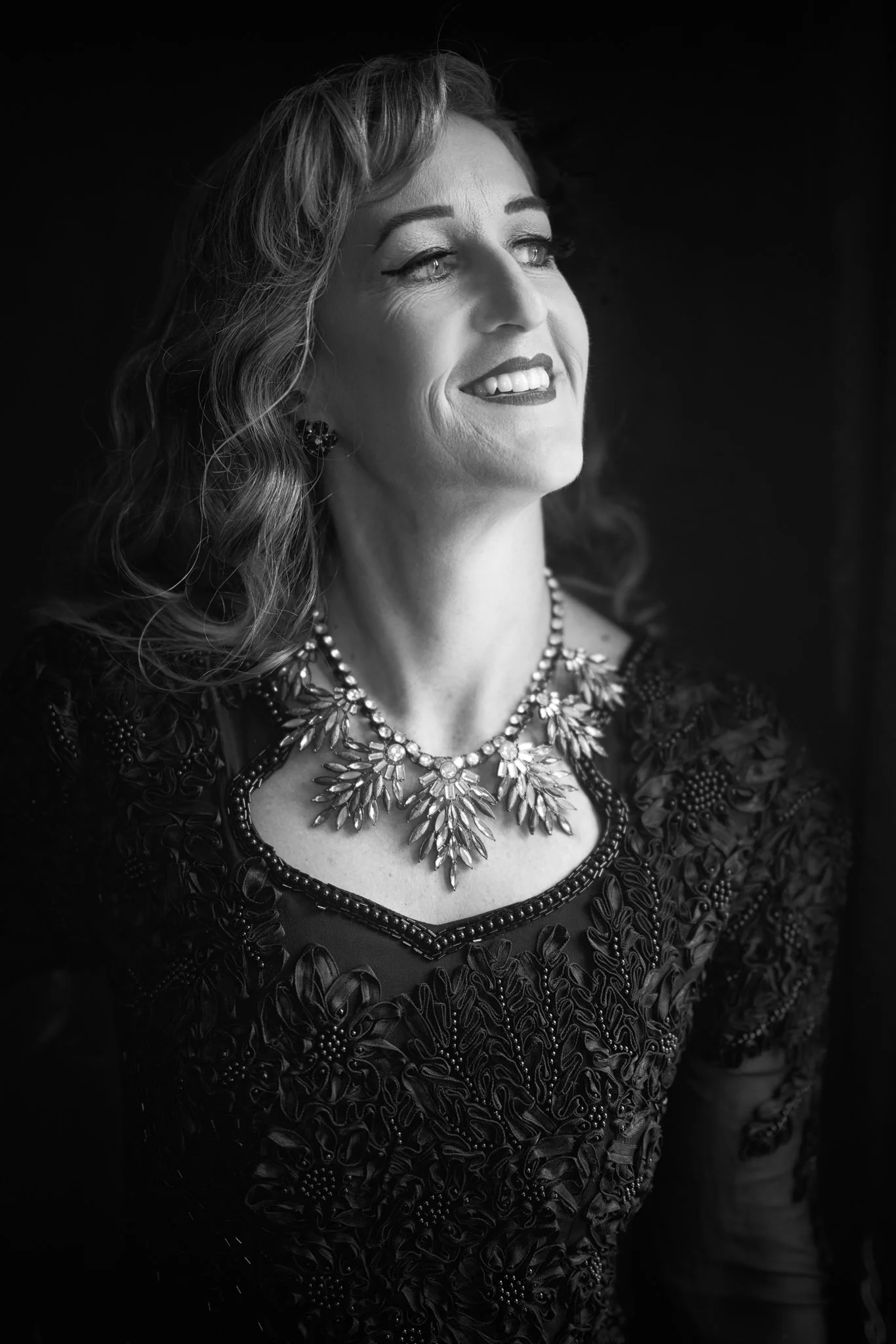 Black and white portrait of Sandy smiling in a statement necklace