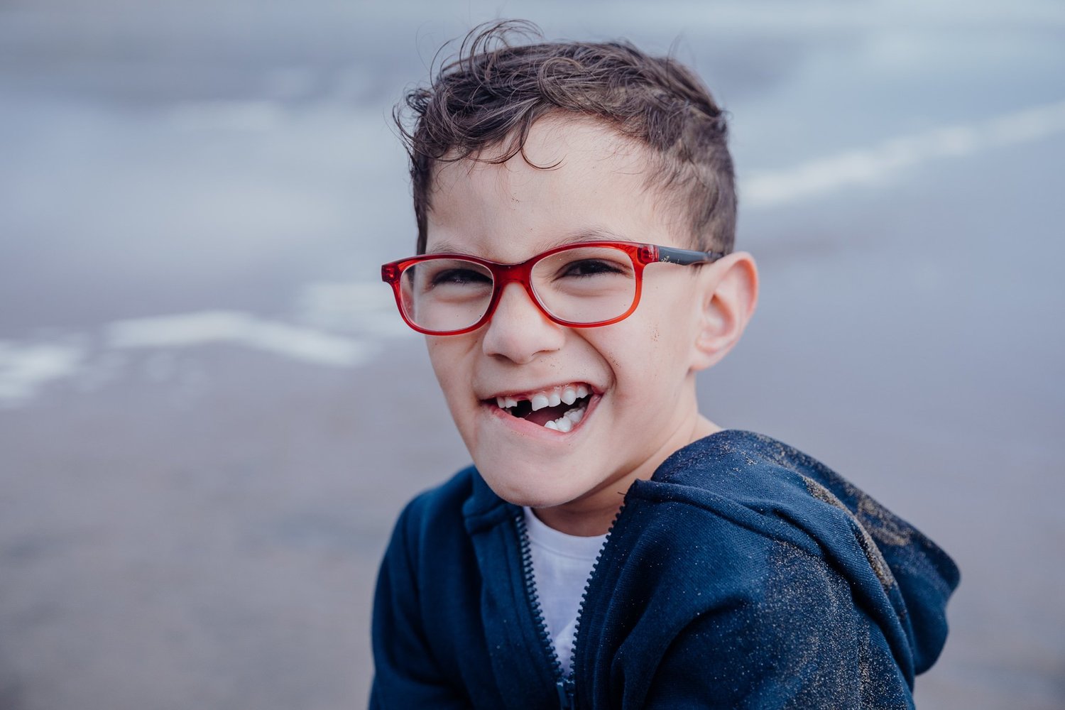 A smiling boy in red glasses on the beach