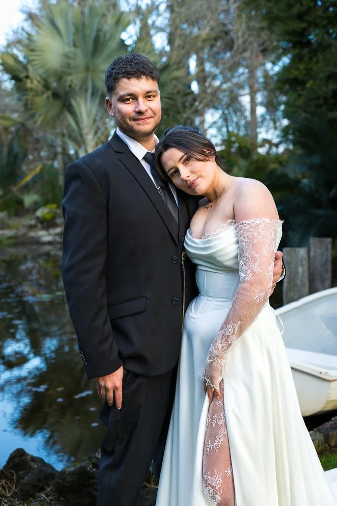 The bride rests her head on the groom's shoulder by the pond
