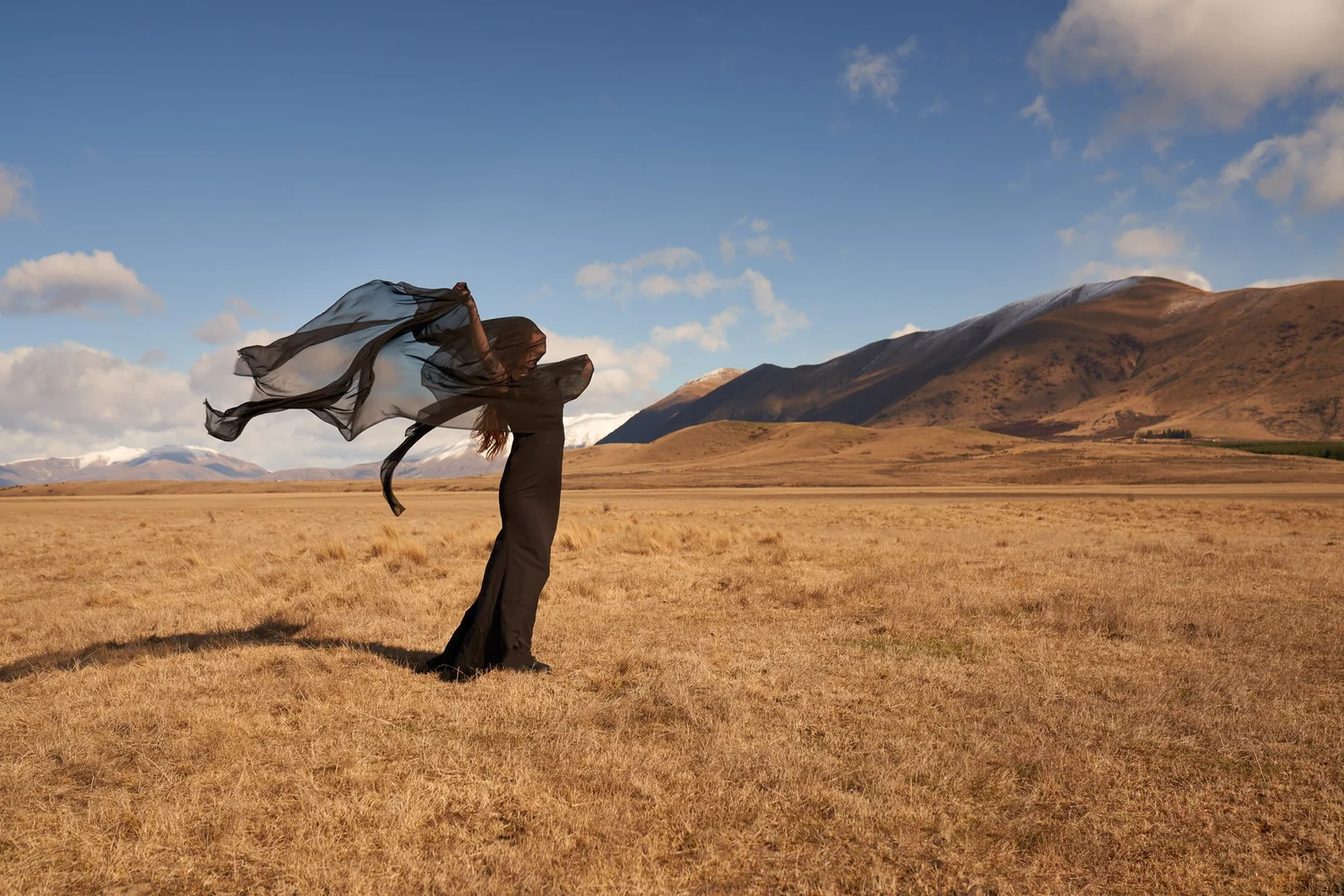 A woman with a flowing scarf in a vast golden valley under blue sky