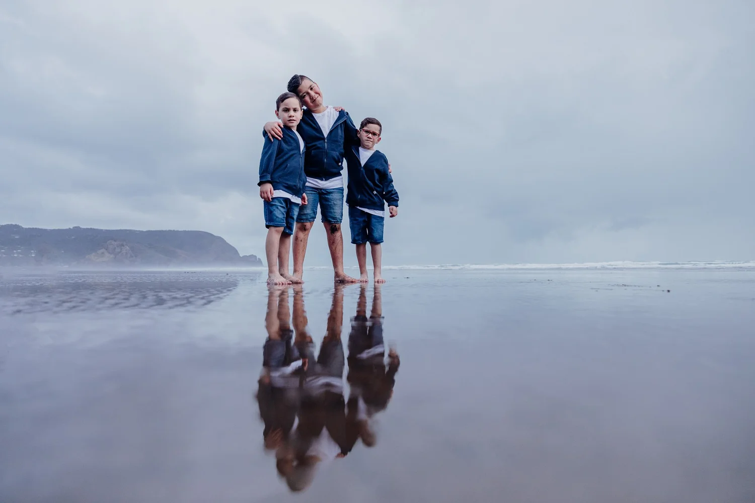 A family reflected in the wet sand on a misty beach