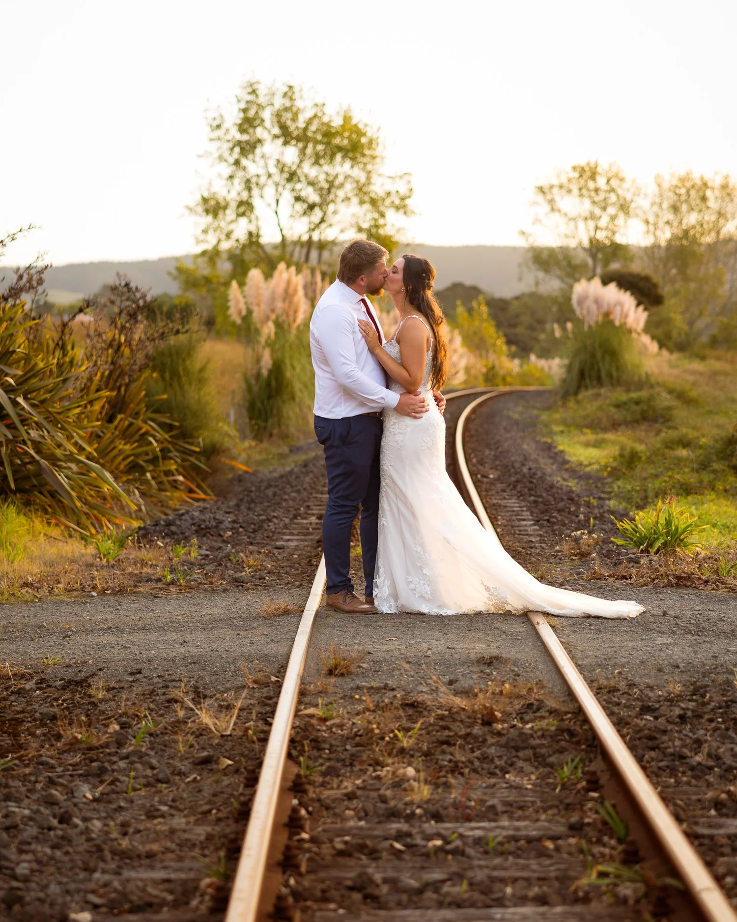 A couple kiss on a railway line in golden light near The Barn Waimauku