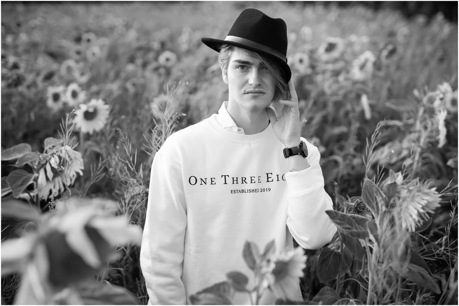 Black and white photo of a young man in a hat among sunflowers