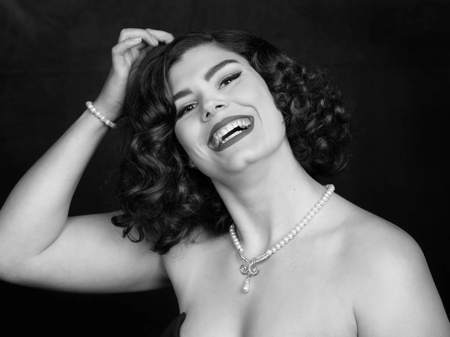Black and white photo of a laughing woman with curls and pearls