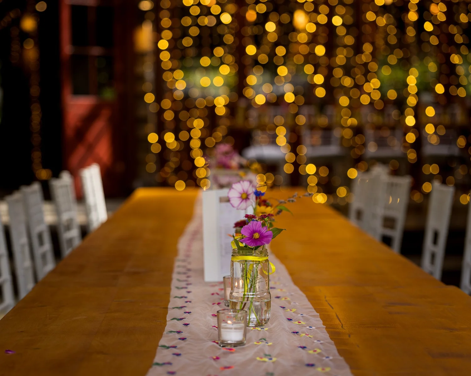 A long reception table with a pink runner and fairy lights