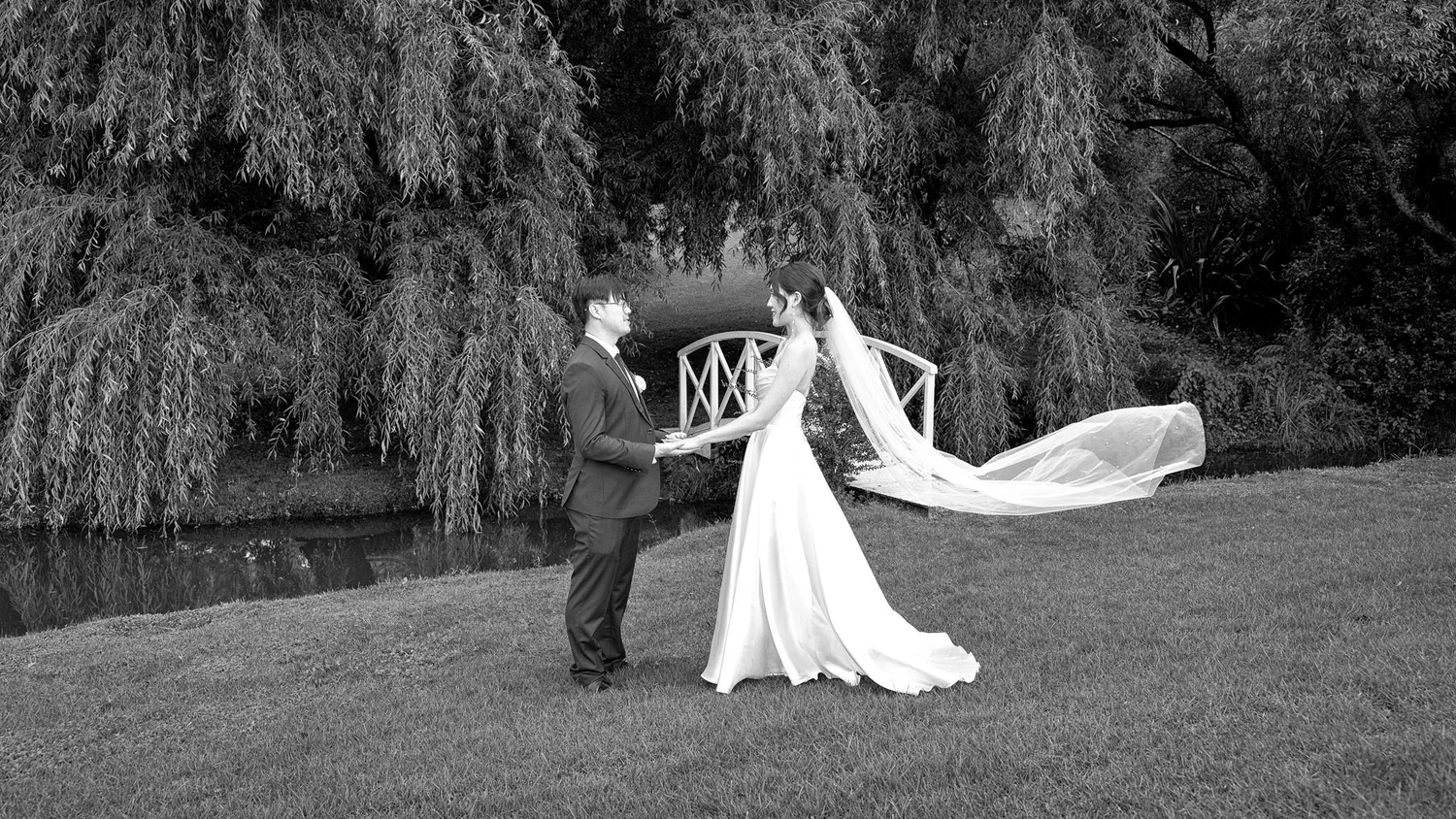 Black and white photo of a bride's veil flowing beside the lake