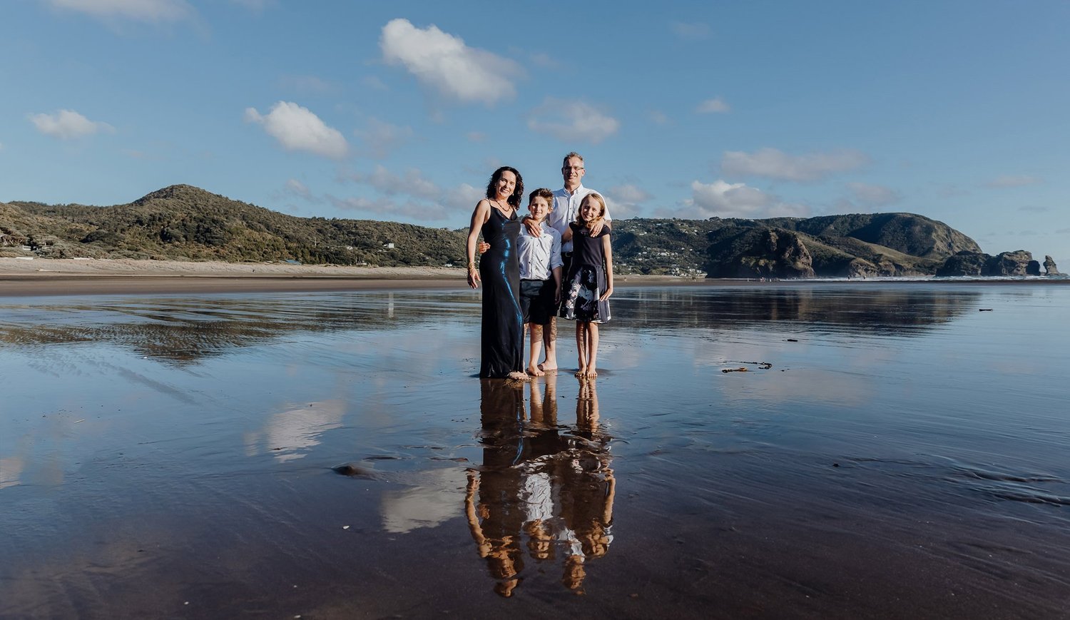 A family standing on reflective sand with headlands behind