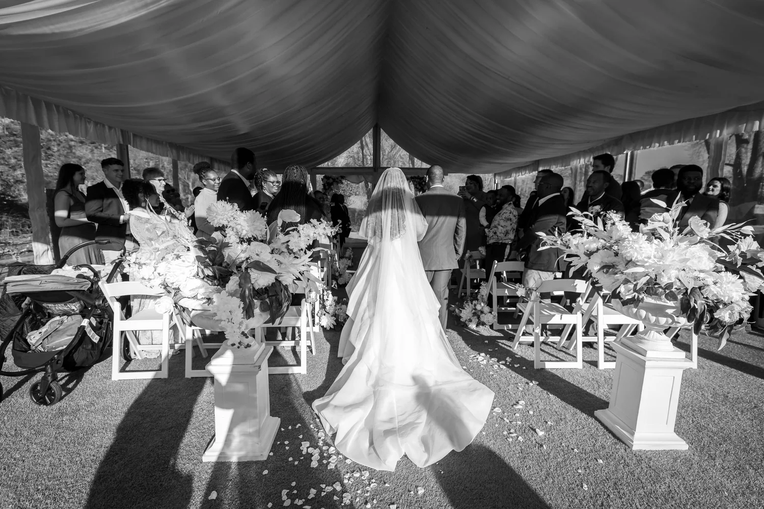 Black and white photo of a bride walking down the aisle in the marquee