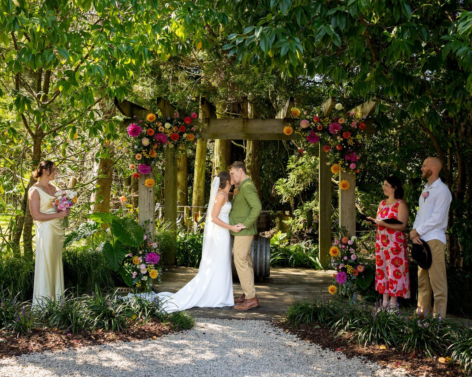 Jade and Ben kiss beneath the colourful floral arch