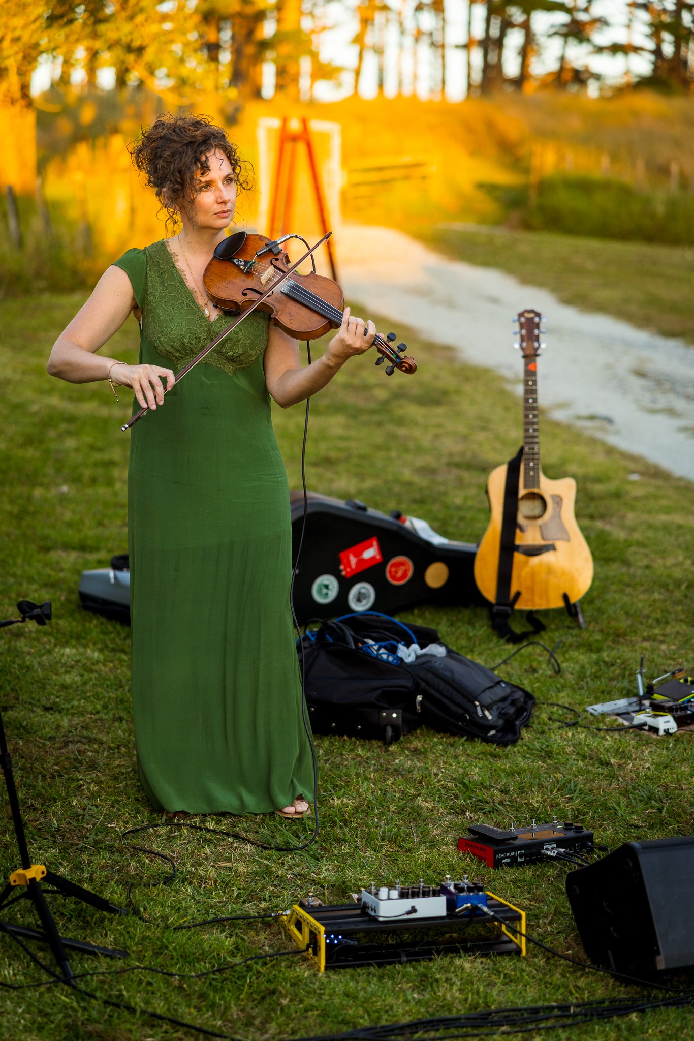 A violinist in green plays on the lawn at golden hour