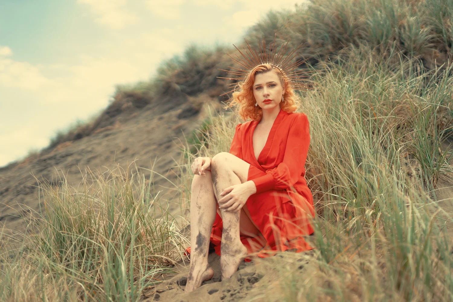 A woman in a red outfit sitting among dune grasses