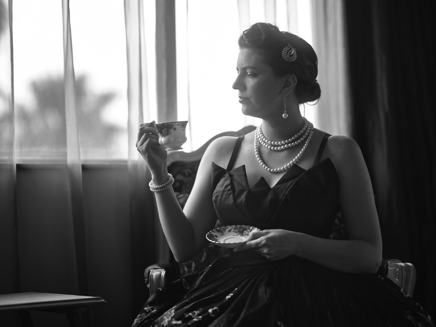 Black and white photo of a woman sipping tea by a window