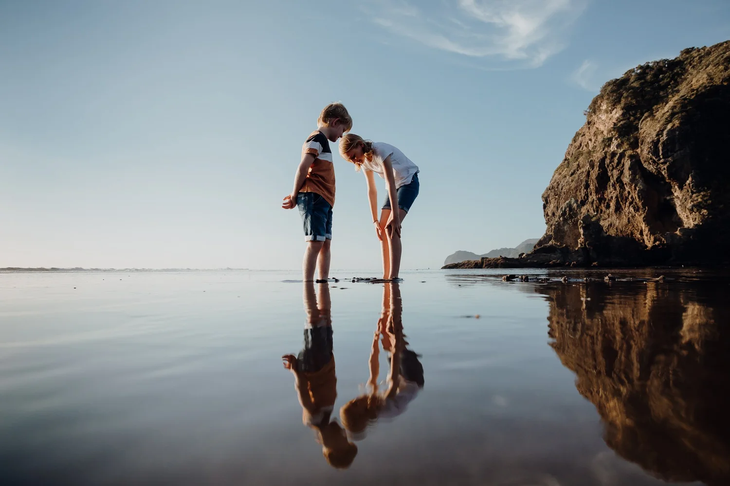 Two children playing on the shoreline at Piha