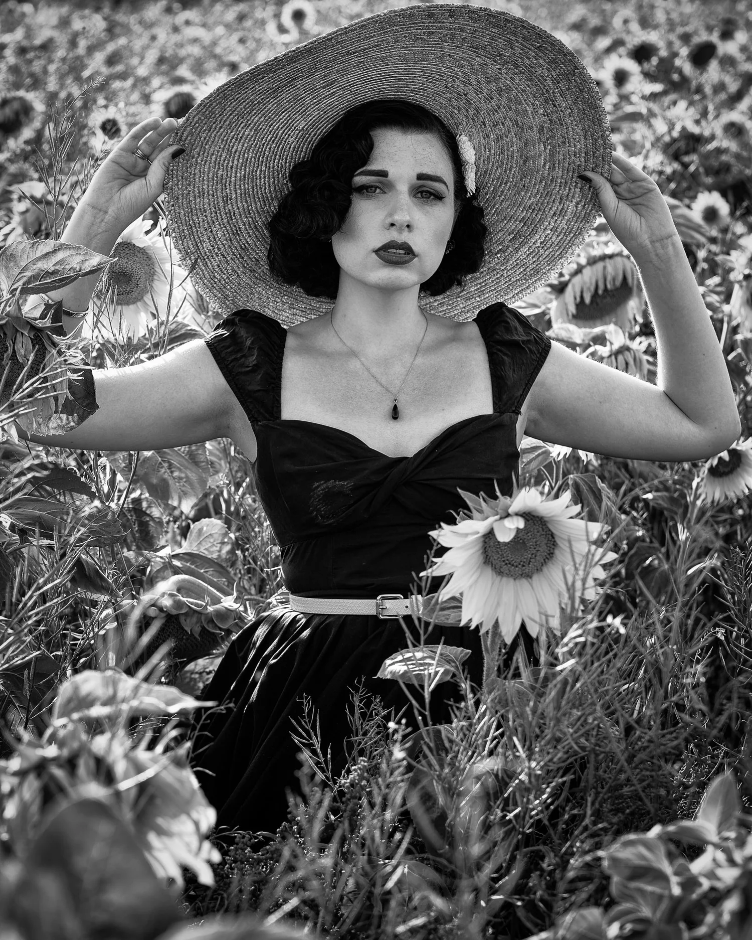 Black and white photo of a woman in a straw hat among sunflowers
