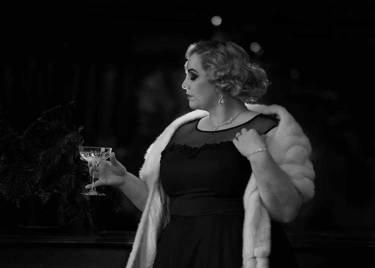 Black and white photo of a woman in a fur wrap holding a cocktail glass