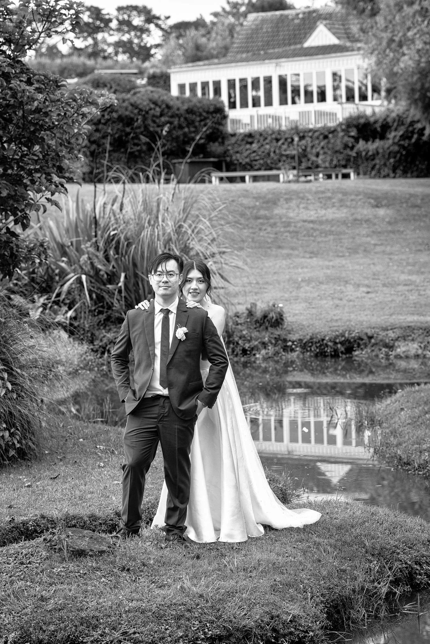 Black and white photo of a couple by the lake with the homestead behind