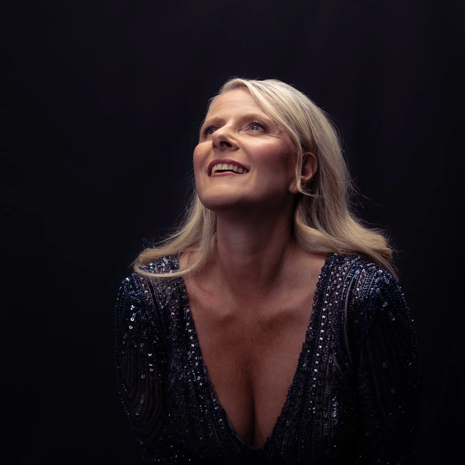 A woman smiles upwards in a sequinned gown