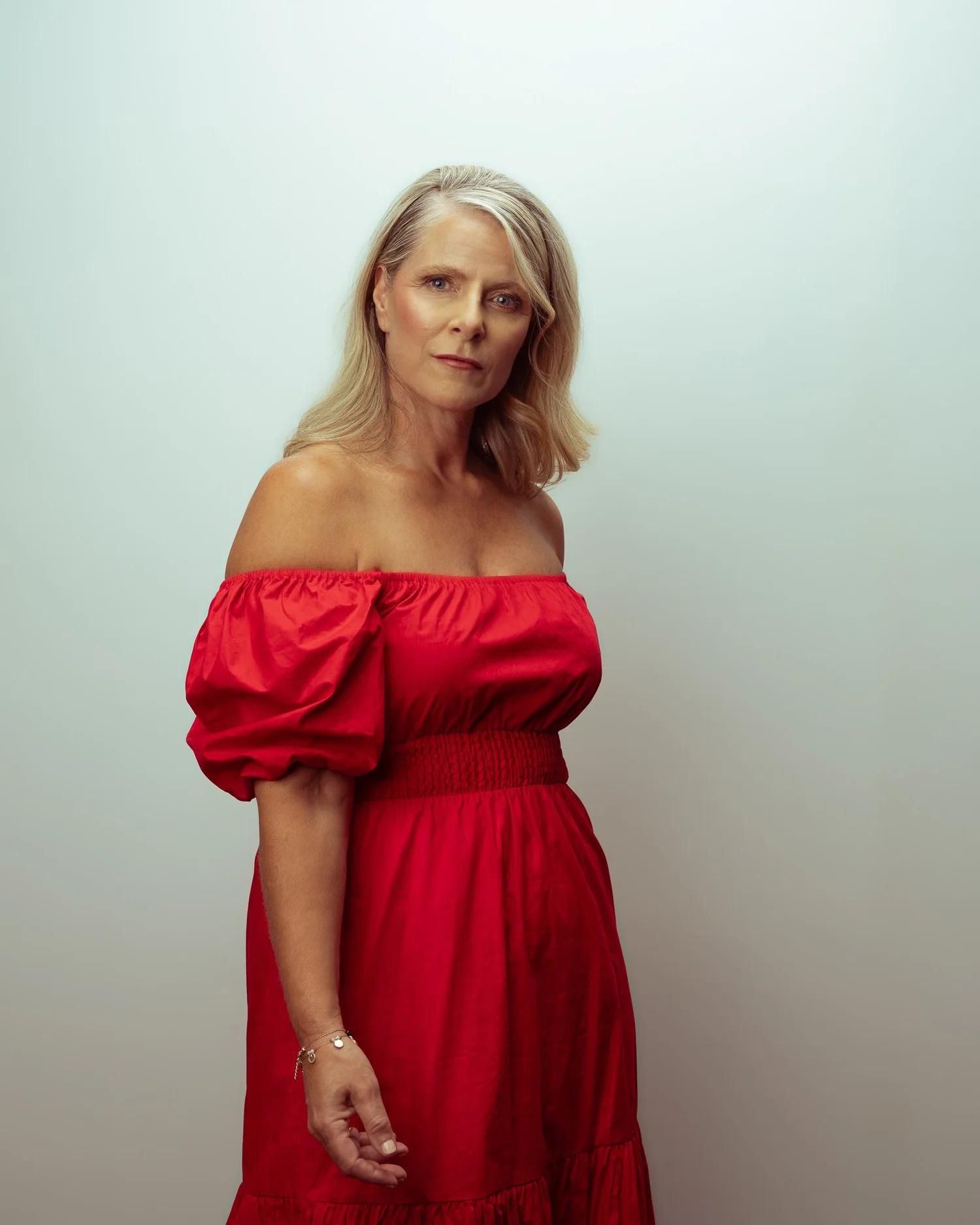 A woman in a red off-the-shoulder dress against a pale backdrop
