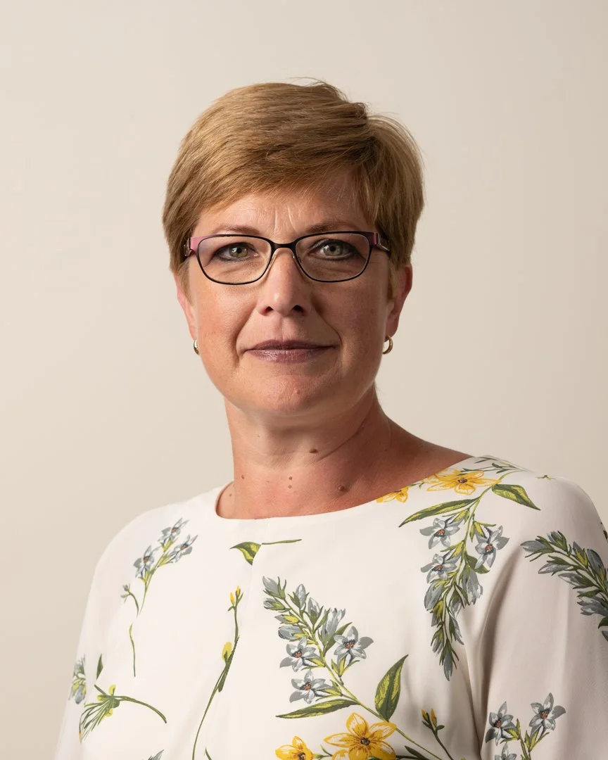A corporate headshot of a woman in glasses and a floral top