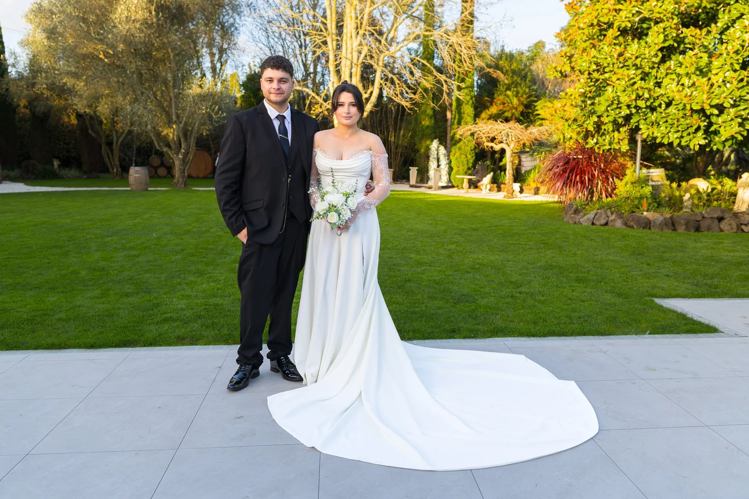 A couple stand on a paved terrace with the gardens behind