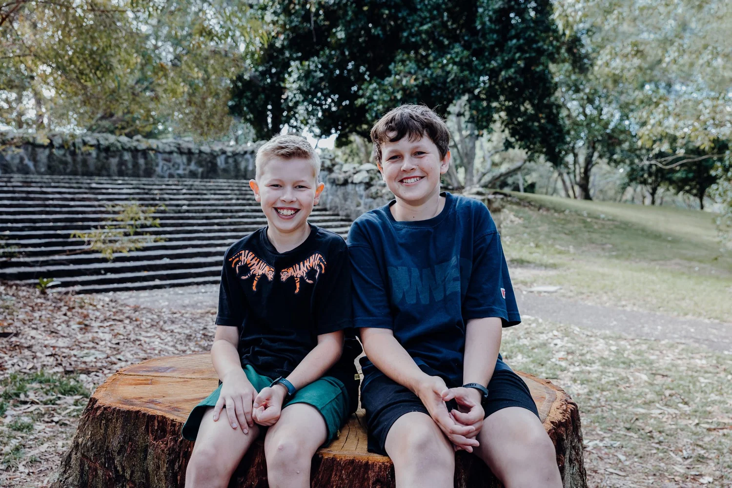 Two brothers sitting on a tree stump in a park
