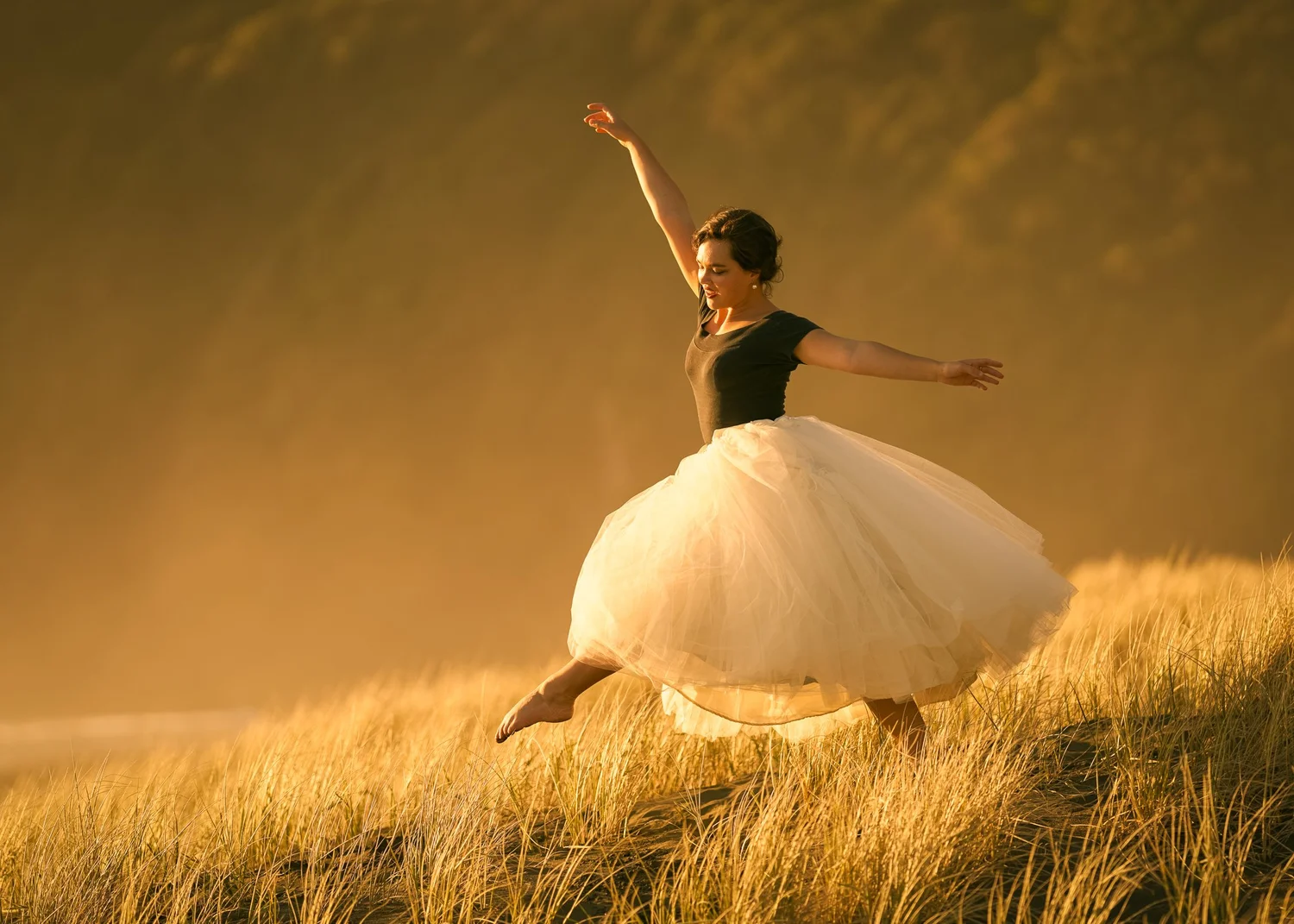 Anita dances in a tulle skirt across golden grass at sunset