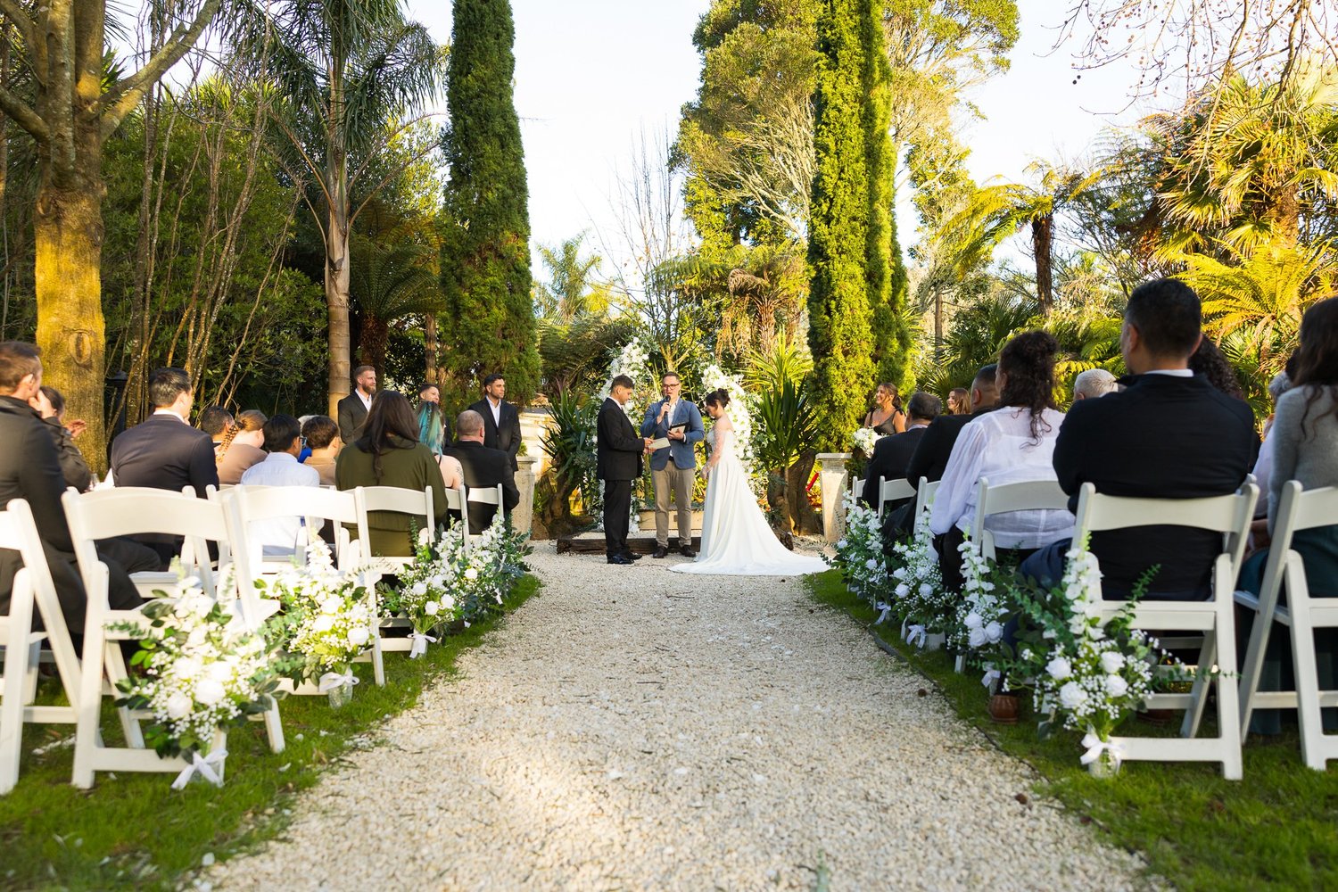 Guests seated either side of a gravel aisle under tall trees
