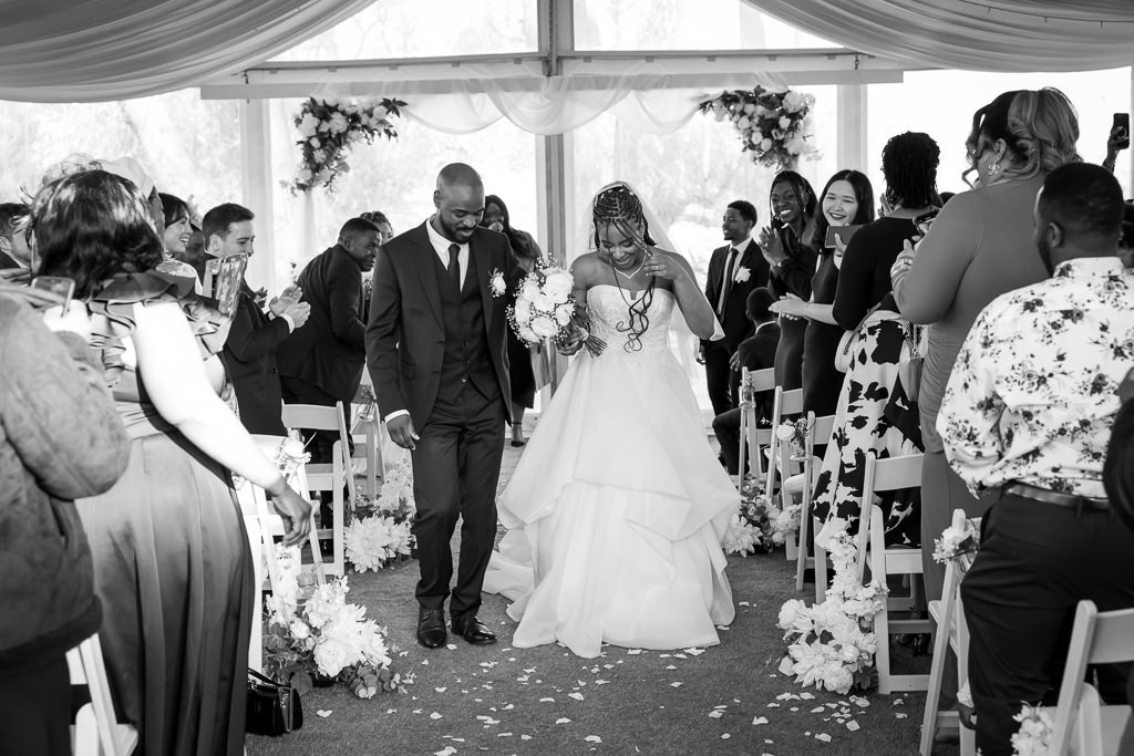 Black and white photo of a couple walking up the aisle past their guests