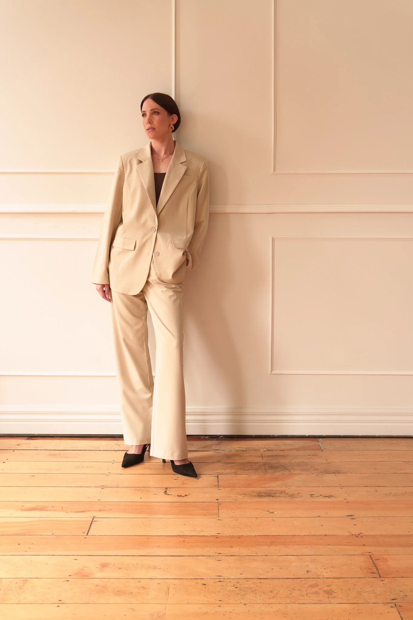 A woman in a cream suit leaning against a panelled wall