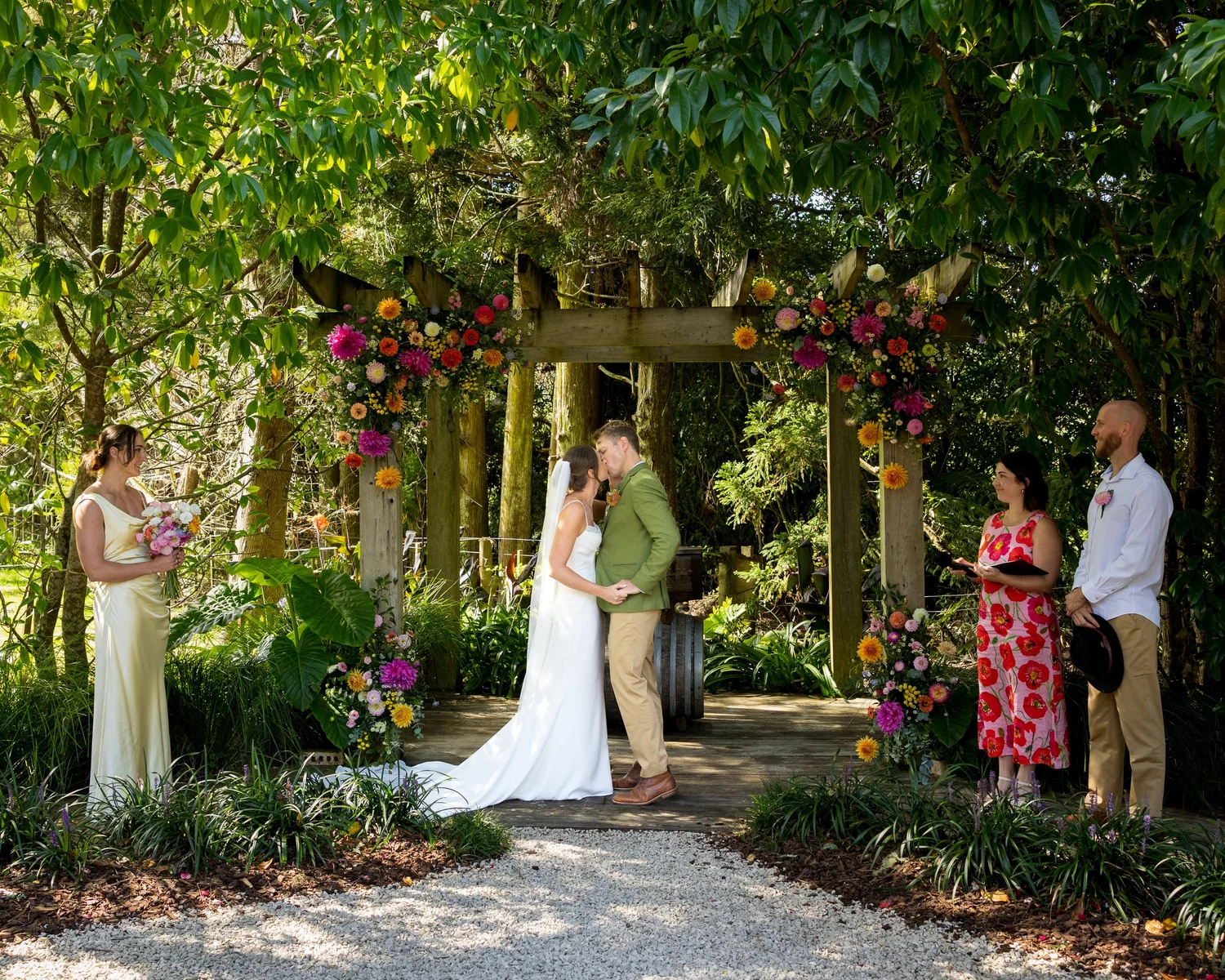Jade and Ben kiss under a flower-covered arch at Kumeu Valley Estate
