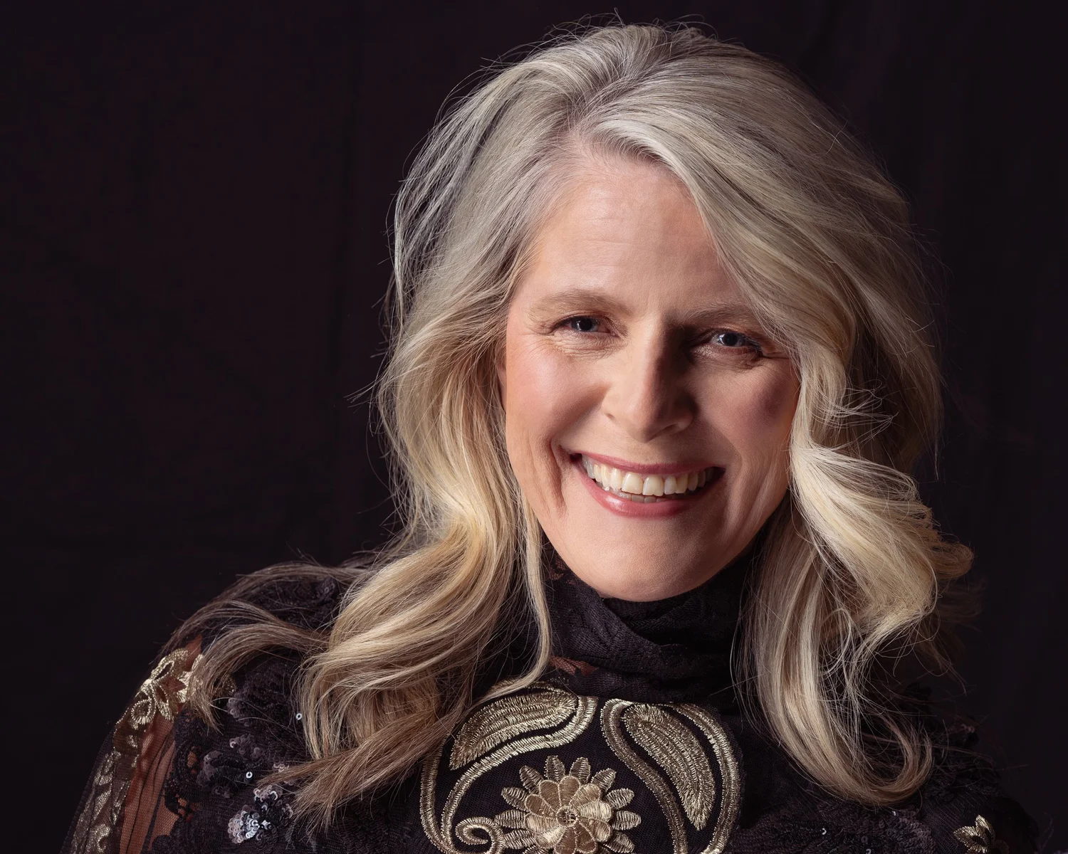 A woman with silver-blonde hair laughing in an embroidered top