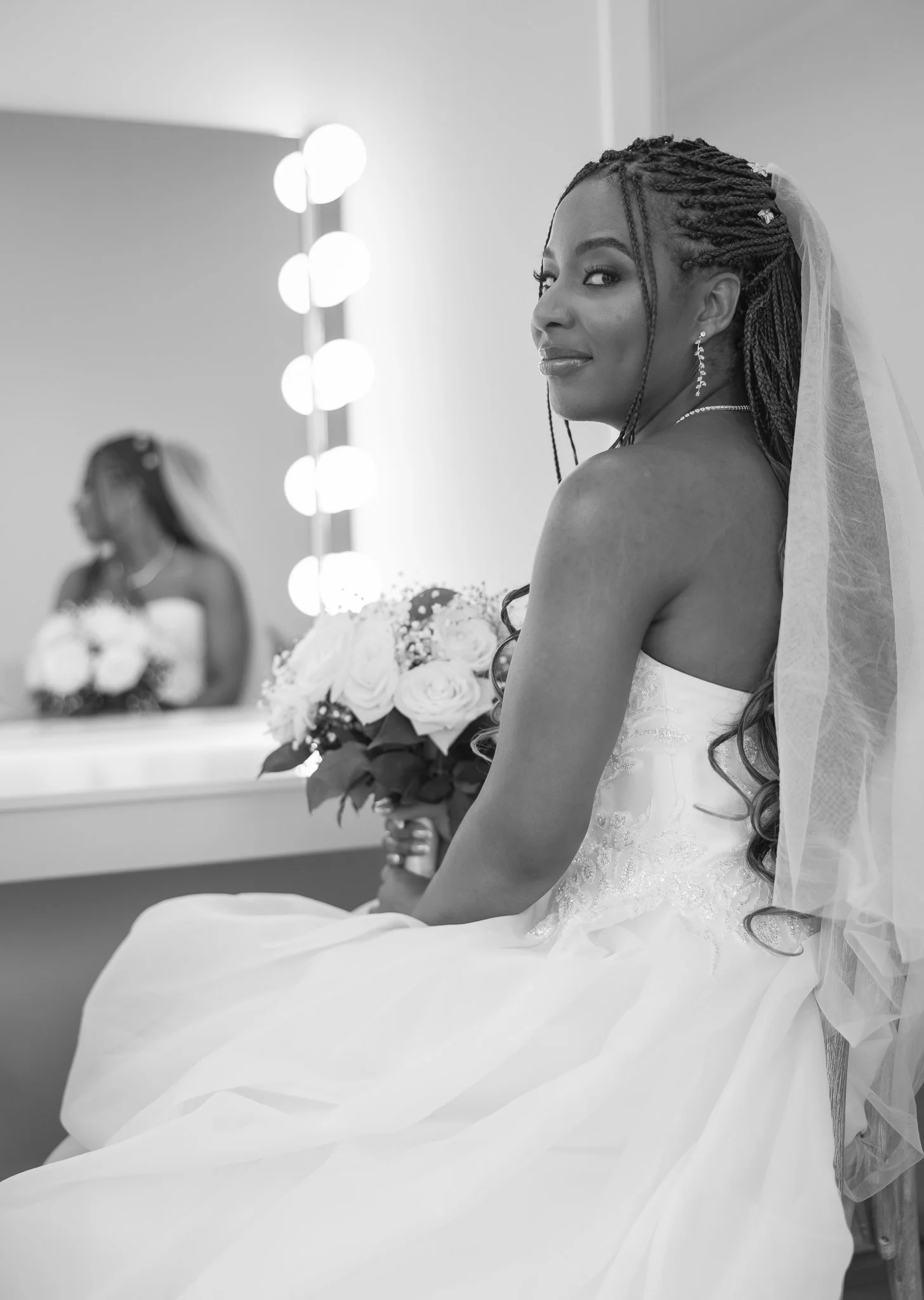 Black and white photo of Chiedza by a lit makeup mirror