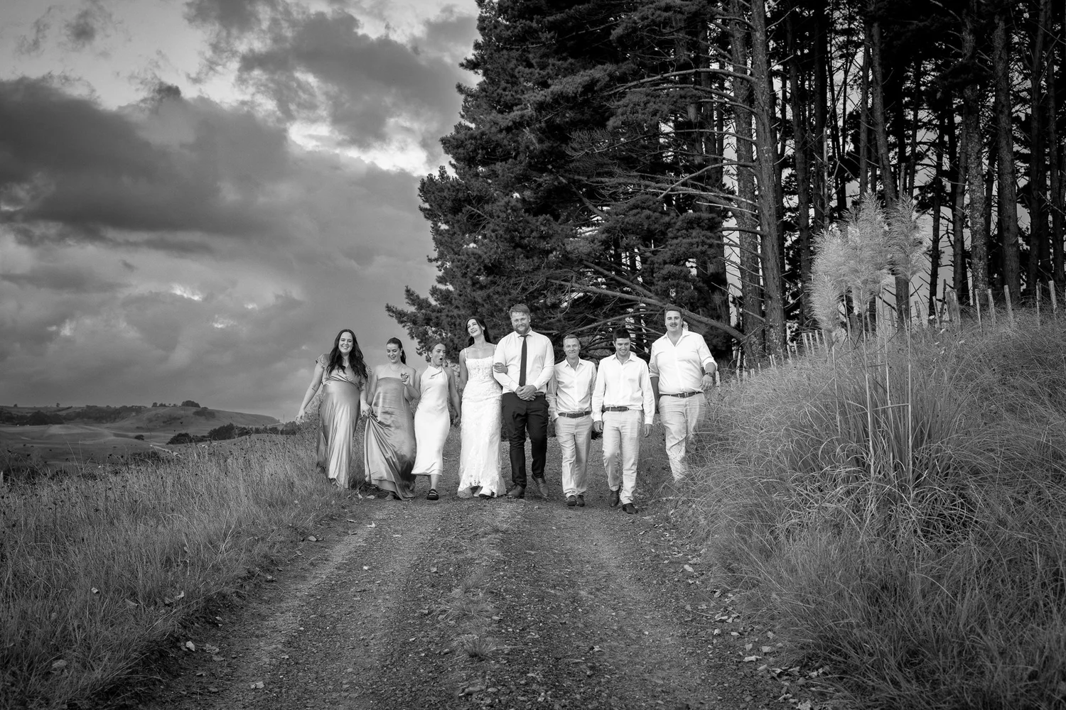 Black and white photo of a bridal party walking along a country road