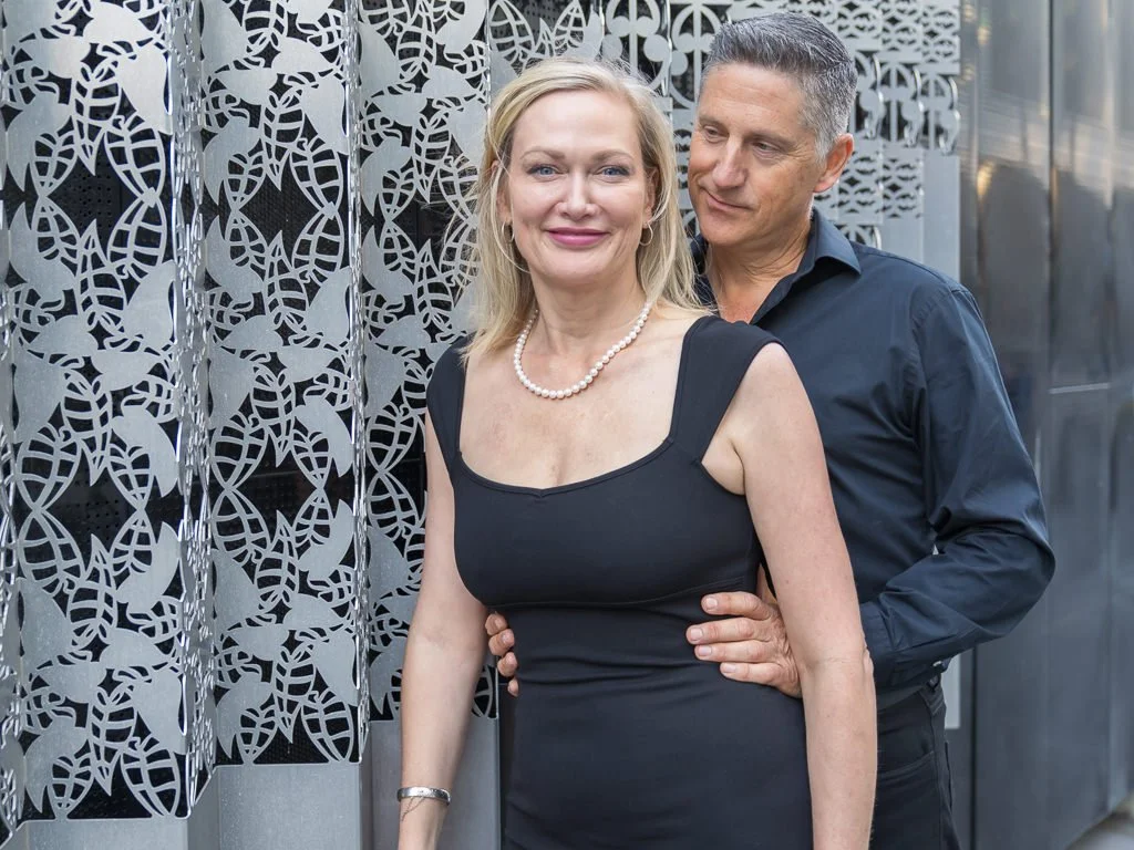 A couple embrace in front of a patterned metal wall in the city