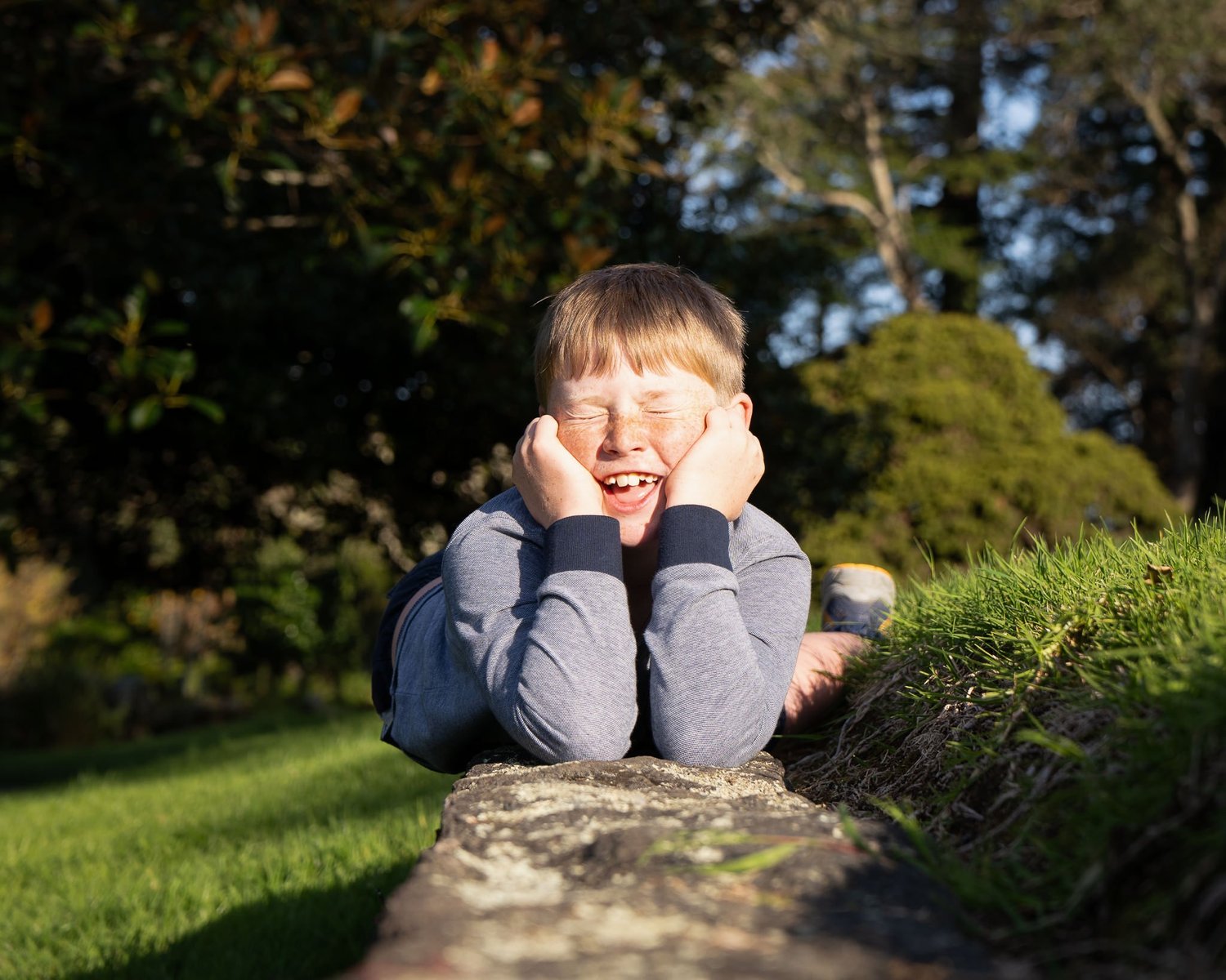 A boy grins resting his chin on his hands on a log